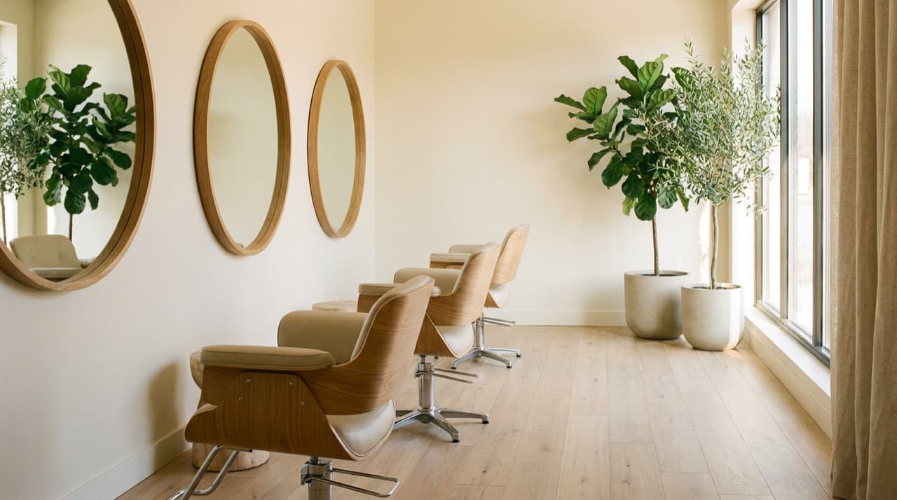 A serene modern beauty salon interior with styling chairs facing backlit mirrors, plants and soft natural daylight